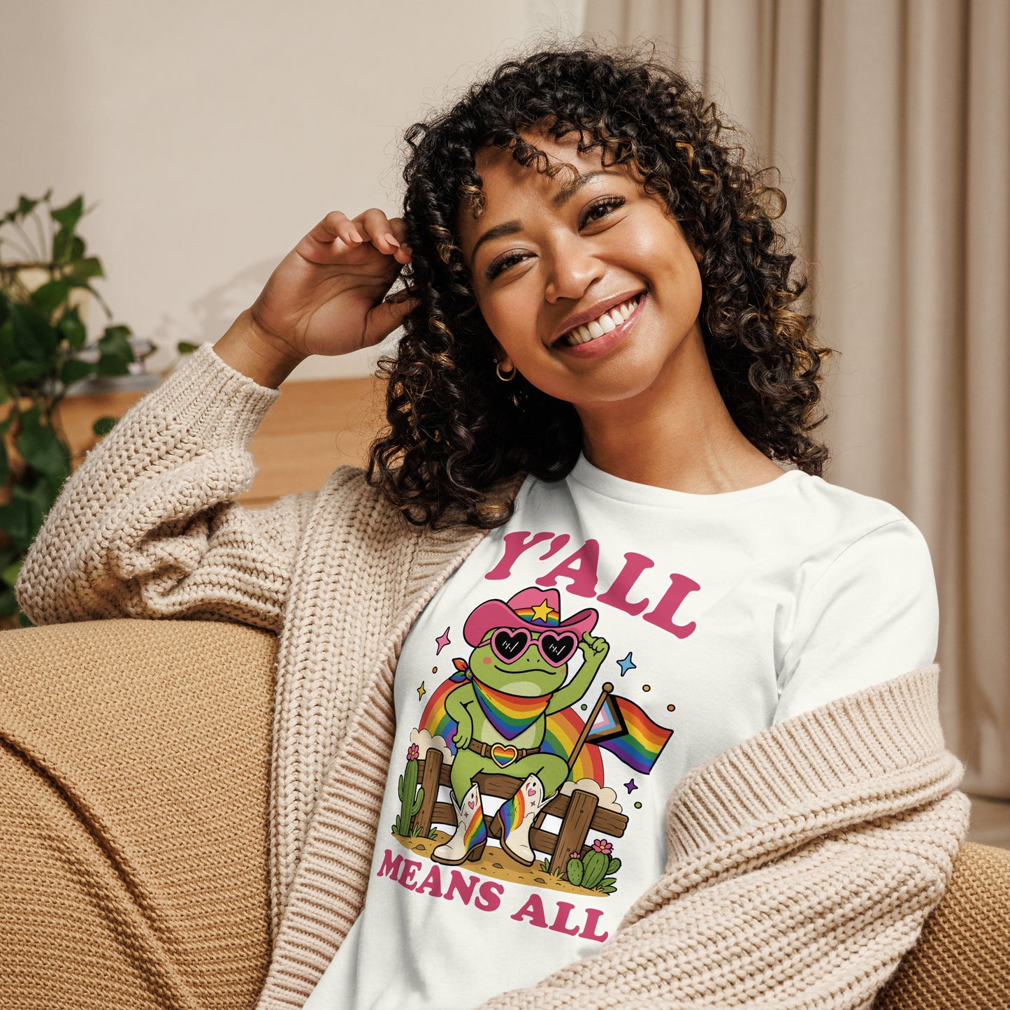 Woman wearing a white women’s relaxed t-shirt featuring a rainbow cowboy frog, pride flag details, and inclusive “Y’All Means All” message celebrating LGBTQ+ pride.